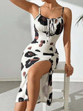 Woman seated on a stool wearing a sleeveless white bodycon dress with bold black and brown abstract print, featuring a front tie detail and a high side slit.